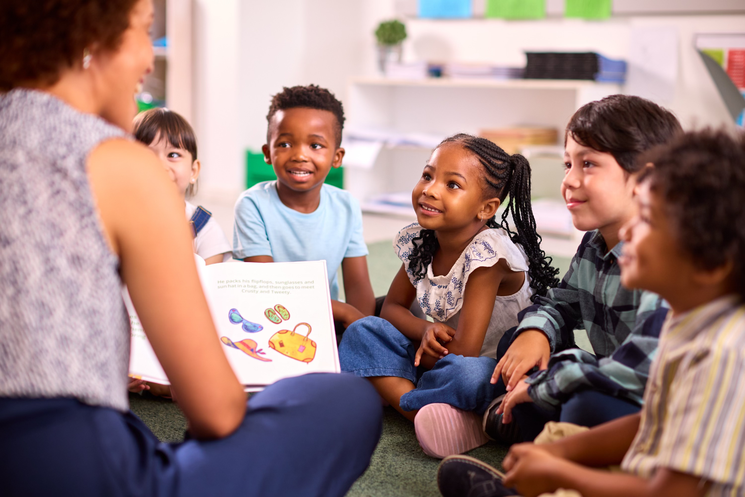 Students sitting down, smiling at teacher who is reading.