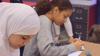 Two girls at their desk, writing on index cards.