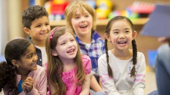 Children sitting on classroom floor, laughing.