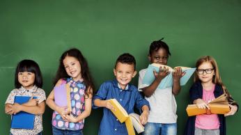 Five kids standing in front of a chalkboard with books in their hands.