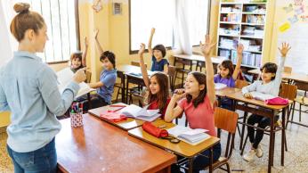 Kids in classroom raising their hands.