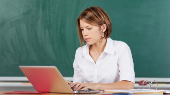 Teacher working on laptop in classroom. 