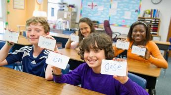 Children in classroom, holding up flashcards.