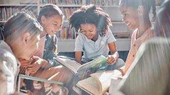 Five diverse students looking happy while reading books in a small circle 