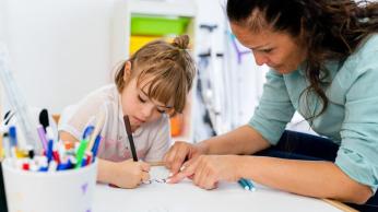 Primary aged girl writing with 1-1 educator next to her providing feedback