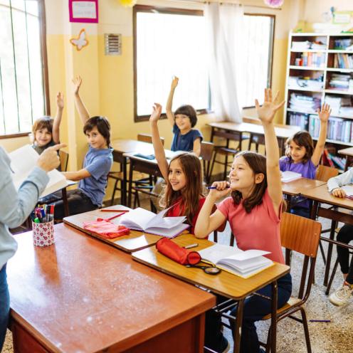 Kids in classroom raising their hands.