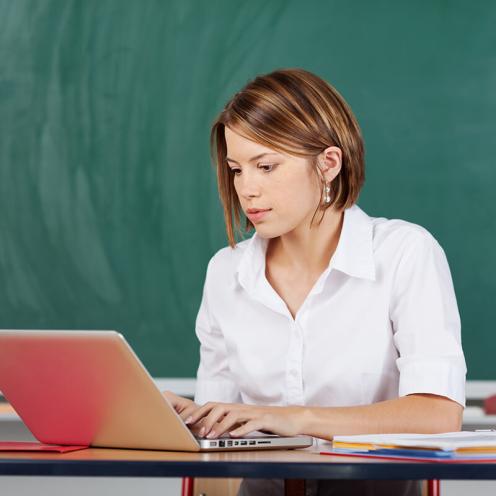 Teacher working on laptop in classroom.