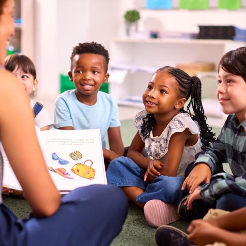 Students sitting down, smiling at teacher who is reading.