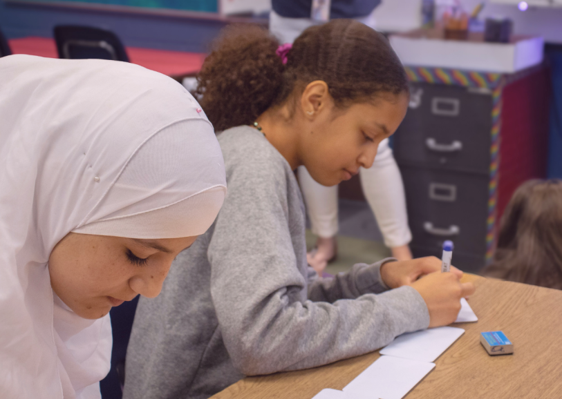 Two girls at their desk, writing on index cards.