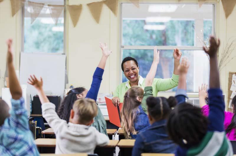 kids raising hands with teacher at front
