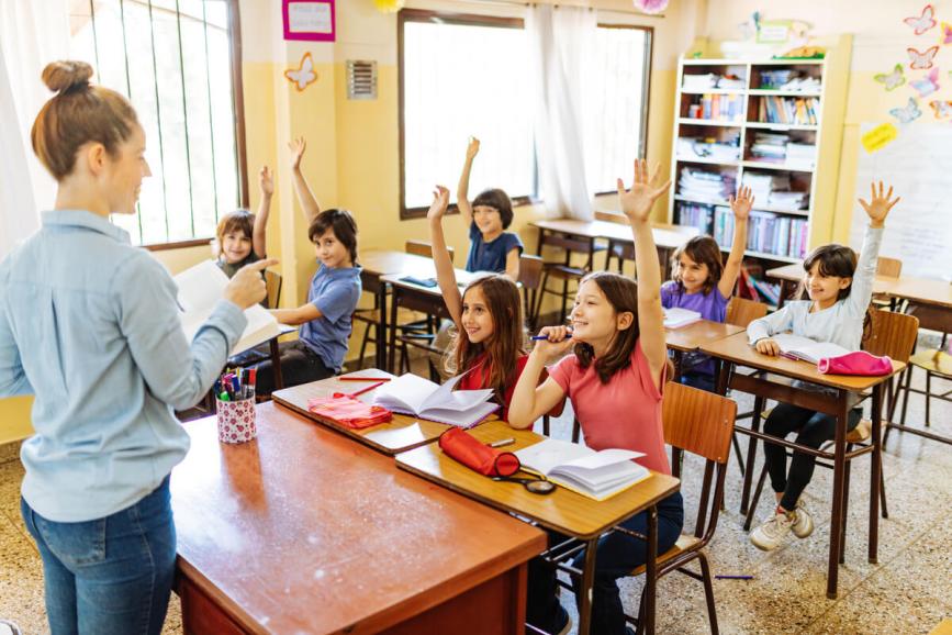Kids in classroom raising their hands.