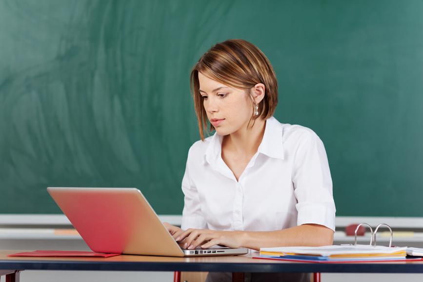 Teacher working on laptop in classroom.