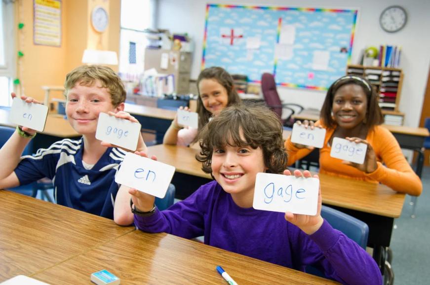 Children in classroom, holding up flashcards.