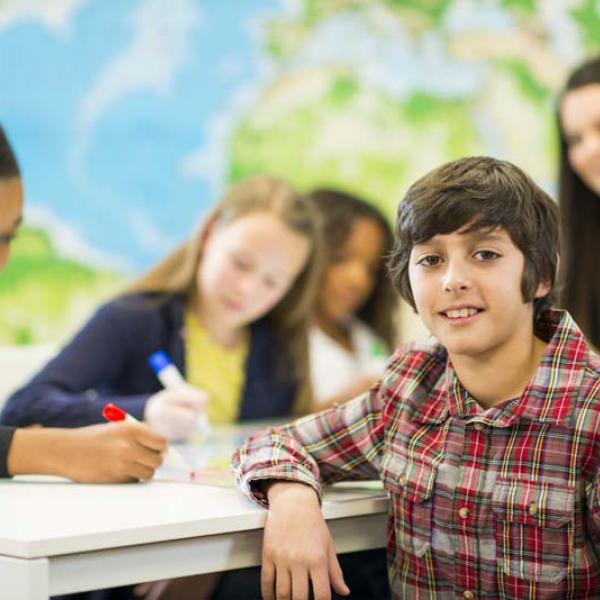 kid looking at camera with other kids in background working with teacher