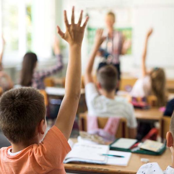back of kids with hands raised with teacher in foreground